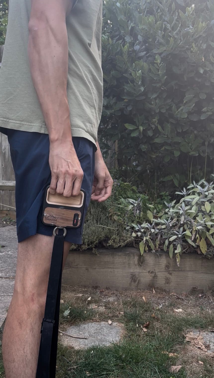 A climber stood on the strap with the LoadCell gripped in one hand at hip height, the strap running taut from the device down under their foot